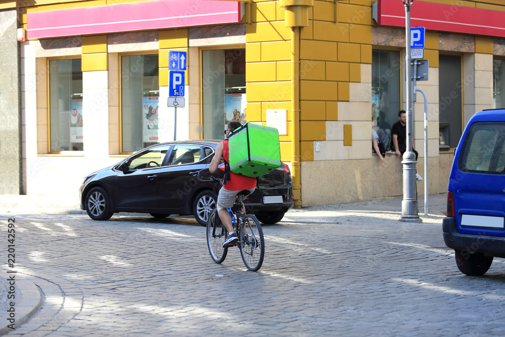 Mężczyzna na rowerze z zielonym kufrem, plecakiem na plecach. - obrazy, fototapety, plakaty 