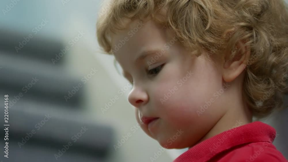 Close up face of adorable little boy with blonde curly hair sitting on stairs at home, using smartphone and looking around Close up face of adorable little boy with blonde curly hair sitting on stairs at home, using smartphone and looking around