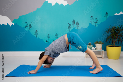 Cute caucasian child does yoga, downward facing dog position, in a beautiful turquoise  room with mountain mural. Adho Mukha Svanasana