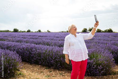 Fototapeta Naklejka Na Ścianę i Meble -  Happy Senior Woman Taking Selfie in Lavender Fields in Provence, France