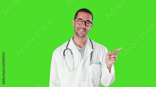Confident young doctor pointing with his finger against green background