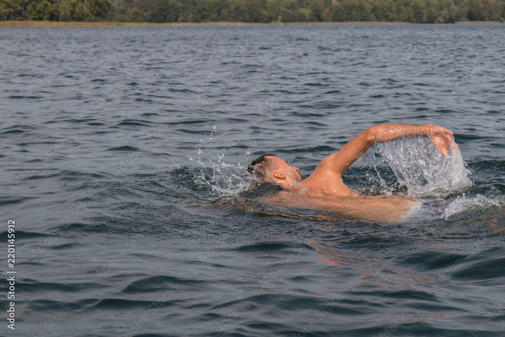 Young man is swimming fast in the lake on a sunny and warm day
