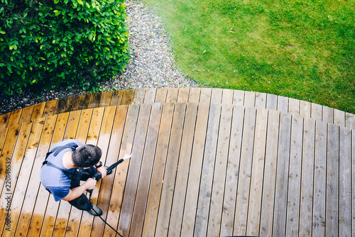 man cleaning terrace with a power washer - high water pressure cleaner on wooden terrace surface