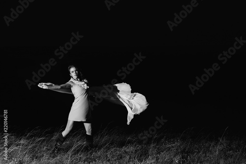 Amazing girl dancing in dress with big white shawl in darkness in grayscale. Beautiful female dancer with good mood in night. Unimaginable mystic dance on nature in dark in monochrome.