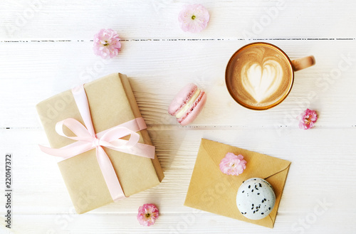 Blueberry and strawberry flavored french macaron desert cakes, brown cappuccino coffee cup, heart shape latte art, craft paper wrapped present tulip flowers. Isolated background, close up copy space