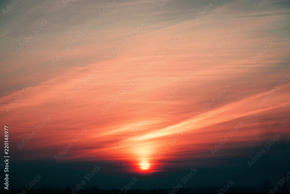 Orange sun circle rises out from behind pink horizon on background varicolored clouds of warmly shades. Beautiful background of majestic dawn on faded cloudy sky. Sun in center.