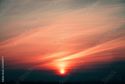 Orange sun circle rises out from behind pink horizon on background varicolored clouds of warmly shades. Beautiful background of majestic dawn on faded cloudy sky. Sun in center. © Daniil