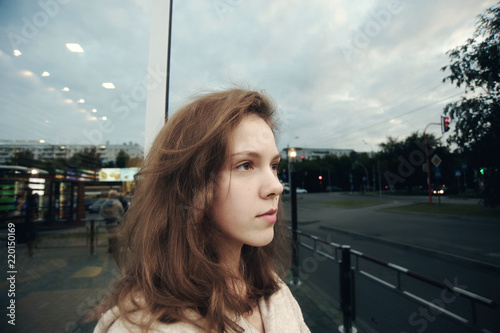Street portrait of fashionable girl with mole on cheek in clothes of vanilla color near reflective window of store. Business woman looking into distance and waiting. Female pensive look.
