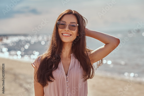 Portrait of a happy beautiful brunette girl with long hair in sunglasses and dress on the beach.