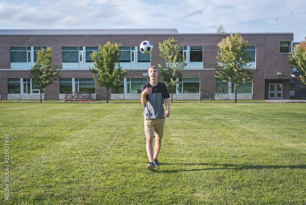 Happy teenager tossing a soccer ball up in the air as he walks through a soccer field.