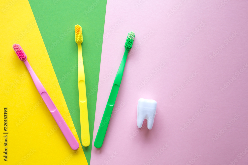 Plastic colorful toothbrushes and white tooth on a yellow, green, pink background. Dental care concept. Plastic colorful toothbrushes and white tooth on a yellow, green, pink background. Dental care concept.