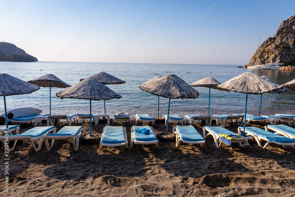 An empty beach in a heavenly bay. Beach umbrellas with sunbeds and towels on towels. Sea and sky background.