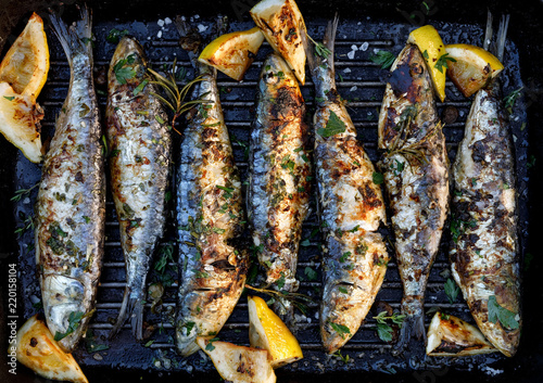 Grilled sardines in a herbal lemon marinade on a grill plate, top view. Grilled food, barbecue
