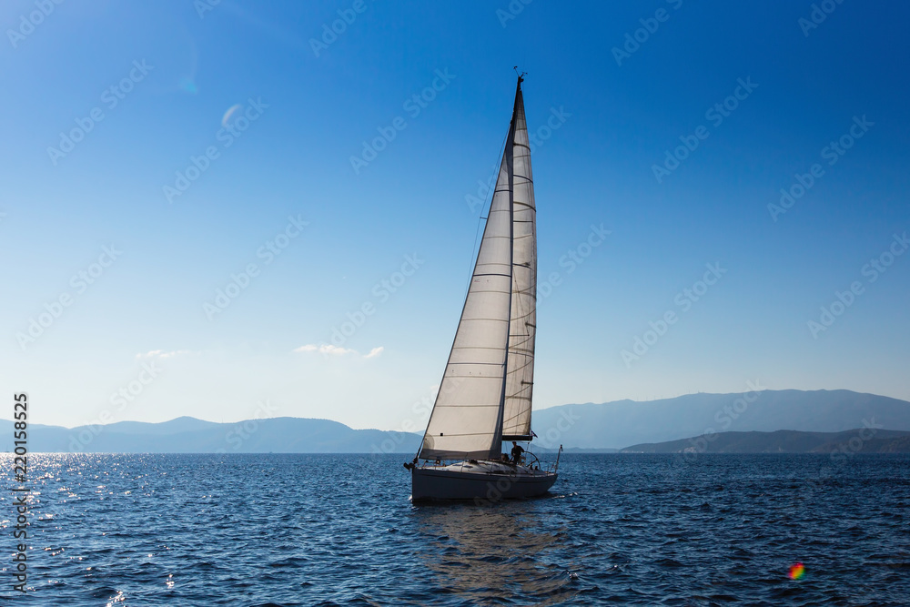 Sailing yacht with white sails in the Sea near Greece coast.