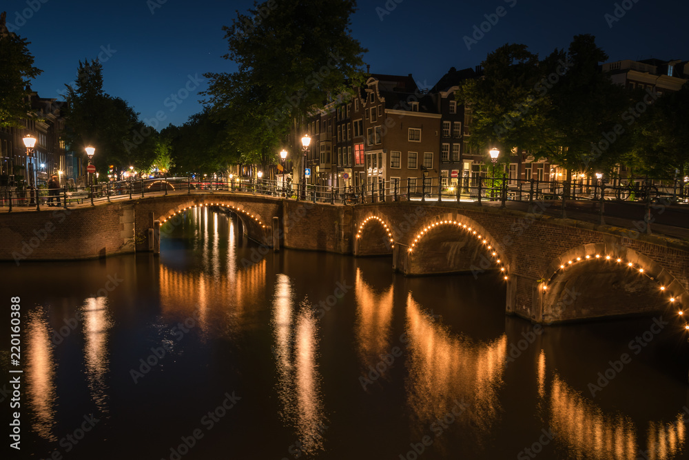 City lights reflected in the canal water at night in Amsterdam, the Netherlands