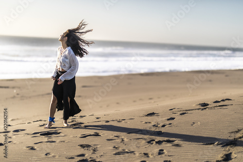 Beautiful young girl walking along the beach sand dunes step by step letting it footprints in the sand. An amazing wild beach during a sunny day at sunset time in Topocalma Beach, Puertecillo, Chile photo