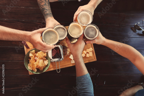 Friends clinking glasses with beer at table, top view
