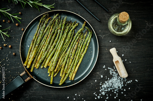 delicious green asparagus in a pan on a wooden black table with rosemary salt and olive oil photo