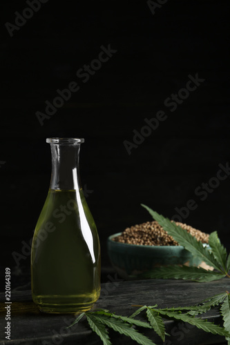 Bottle with hemp oil and fresh leaves on dark table. Space for text