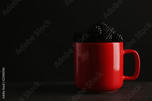 Mug with fresh blackberry on gray table against dark background. Space for text