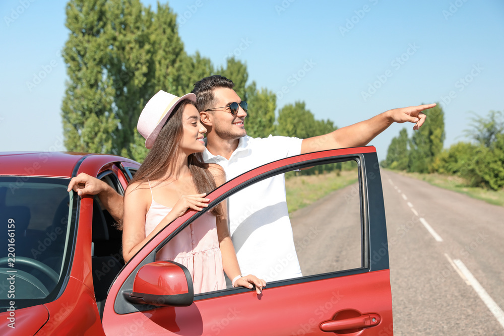 Naklejka premium Happy young couple standing near car on road