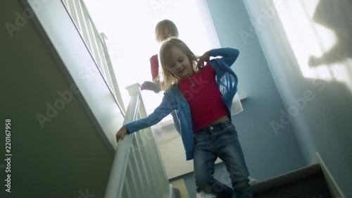 Dutch angle view of two playful little girls of elementary school age running downstairs when spending time together at home, slow motion