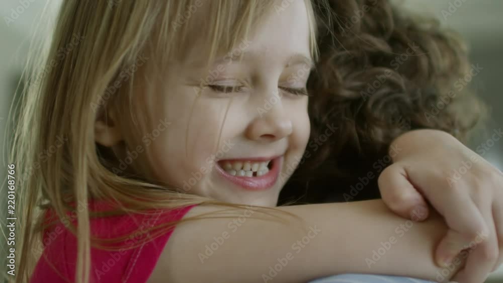Close up face of happy affectionate little girl of primary school age smiling and hugging mother Close up face of happy affectionate little girl of primary school age smiling and hugging mother