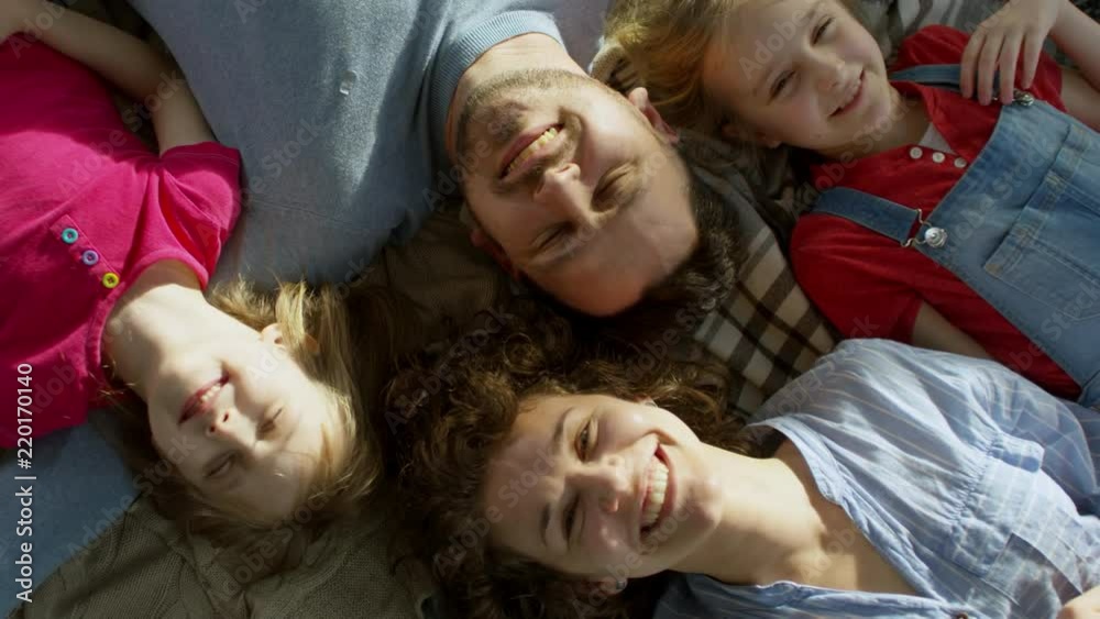 Top view of family with two children of elementary school age lying together on floor or bed and smiling at camera Top view of family with two children of elementary school age lying together on floor or bed and smiling at camera