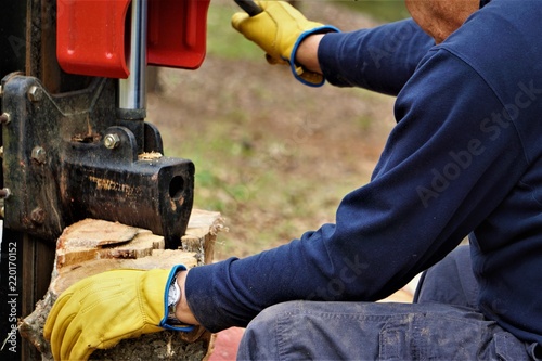 A man working with the firewood to split the logs by the machine on the driveway in the garden, Winter in GA USA.