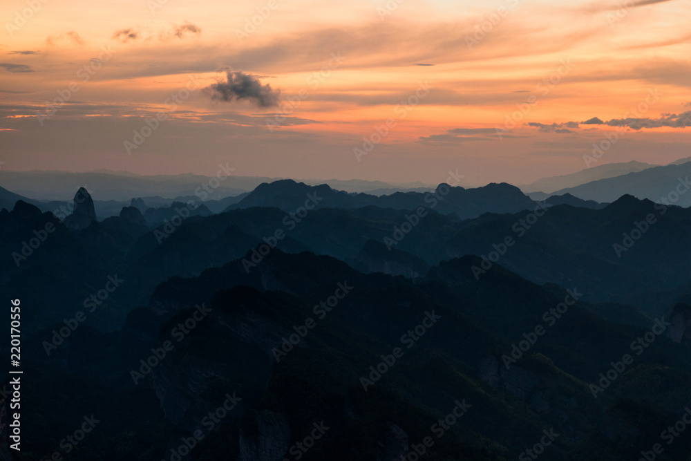 Bajiaozhai National Forest Park in Ziyuan County, Guangxi Province China. Dawn, Orange Sunrise, and Danxia Landform Silhouettes. Rugged Mountains, Danxia Cliffs, Candle Peak in the Distance. Abstract