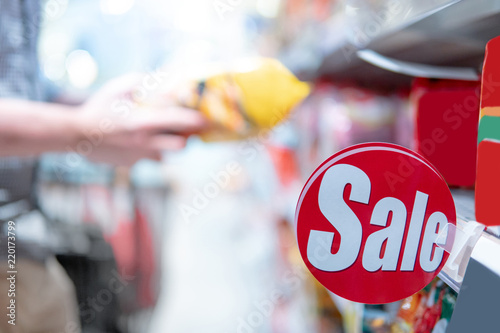 Red sale label on product shelf in supermarket with blurred male hand shopper choosing food package in the background. shopping lifestyle in grocery store concept