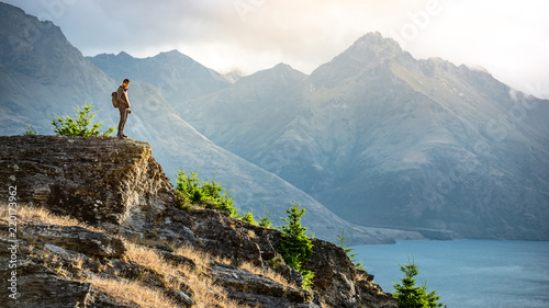 Young male photographer looking at mountain scenery during golden hour sunset in Queenstown, South Island, New Zealand. Travel and photography concept photo