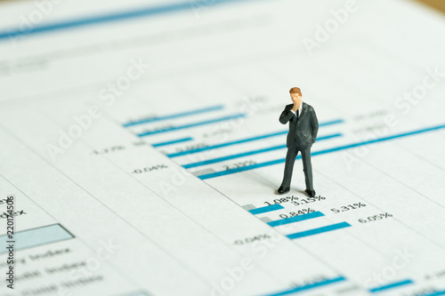 Investment, financial performance report analysis concept, miniature people figurine success businessman standing and thinking on printed stock exchange data graph and chart document © Nuthawut