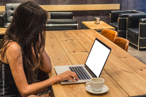 A woman working on her computer on a coffee shop or co working space. She is wearing a tank top and she has a backpack next to her. Digital nomad concept.