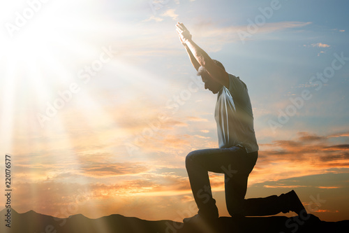 Man Kneeling And Praying At Sunset