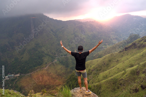 Carefree happy man enjoying nature and sunrise standing on top of mountain cliff