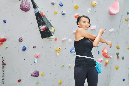 Pretty Vietnamese woman warming-up before bouldering on artificial wall