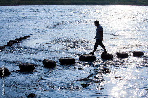 Man walking on stepping stone over river