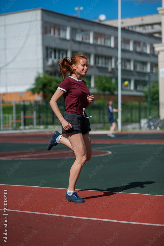 Red-haired young girl runs in the stadium. Student delivers standards for running outdoors. Young woman running on the football field