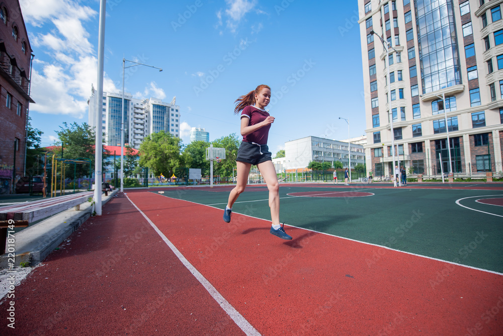 Red-haired young girl runs in the stadium. Student delivers standards for running outdoors. Young woman running on the football field Red-haired young girl runs in the stadium. Student delivers standards for running outdoors. Young woman running on the football field