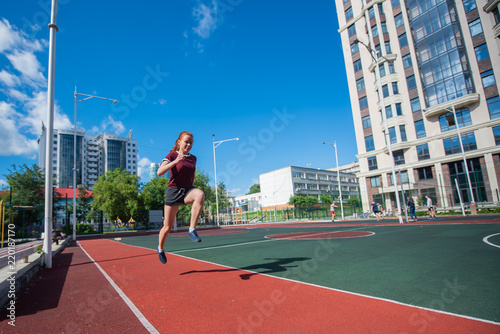 Red-haired young girl runs in the stadium. Student delivers standards for running outdoors. Young woman running on the football field