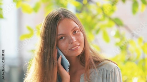 Beautiful young pretty girl in blue shirt with phone in blue case talking outdise on a summer day stable shot photo