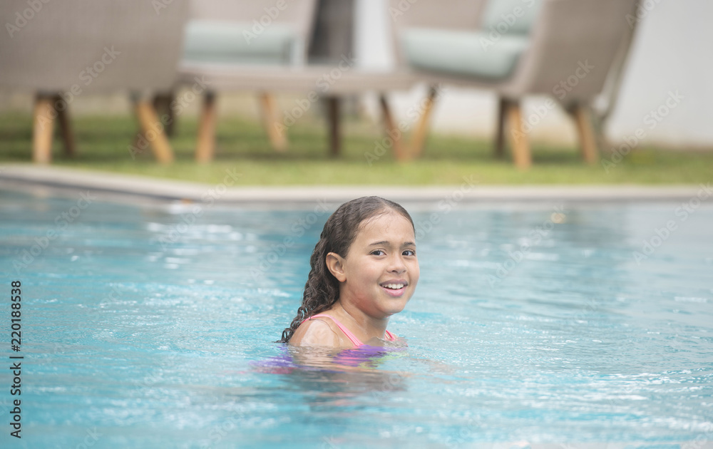 Young child with a big smile relaxing, swimming and playing calmly in a pool showing her wet curly hair