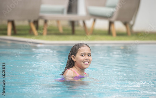 Young child with a big smile relaxing, swimming and playing calmly in a pool showing her wet curly hair © Paul