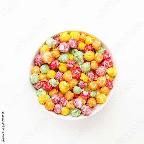 Sweet yellow  purple  green  orange and red popcorn in a bowl on a white table. Multicolored delicacy with different tastes. Top view.