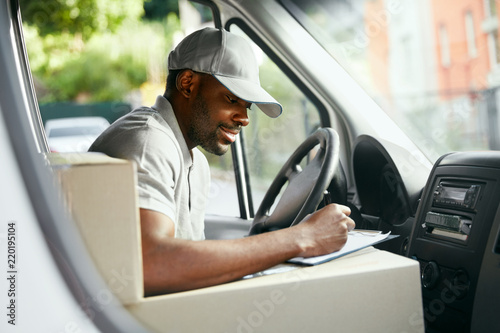 Courier. Delivery Man Reading Addresses Sitting In Delivery Van