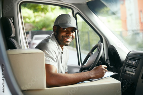 Fototapeta Courier Delivery. Black Man Driver Driving Delivery Car