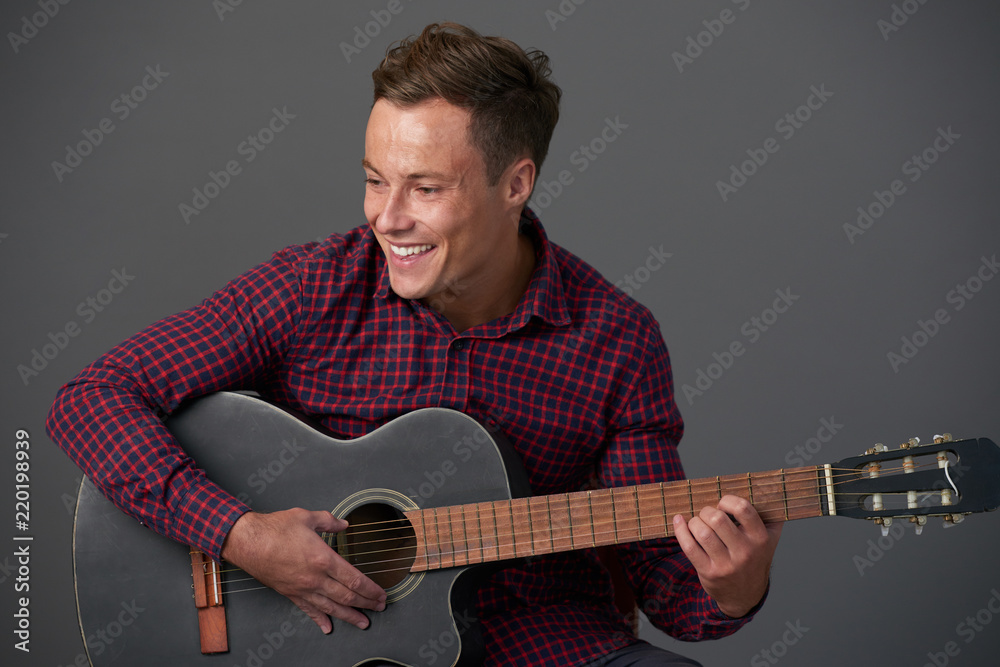 Obraz premium Happy young man in plaid shirt playing acoustic guitar