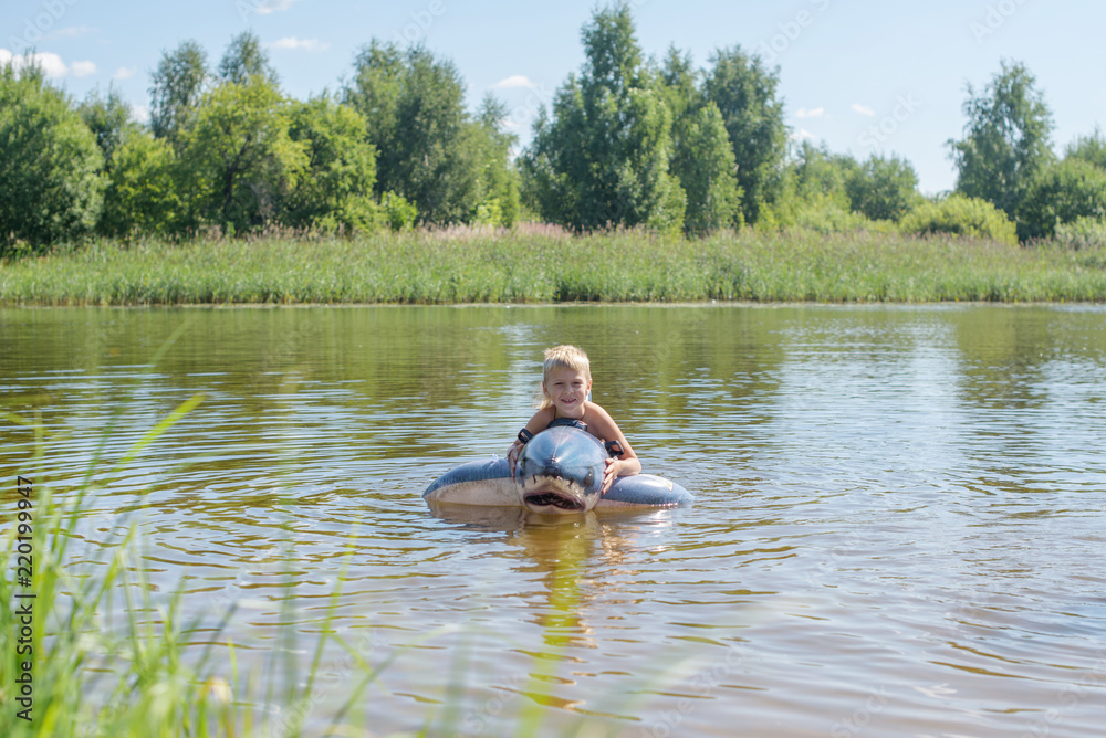 little boy swimming in the river on an inflatable shark little boy swimming in the river on an inflatable shark