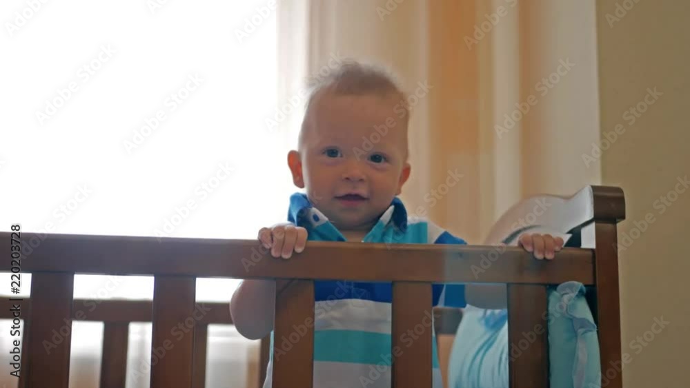 Baby standing in bed at home. Portrait of baby boyl stand in cot. Baby eyes looking for mother. Baby standing in bed at home. Portrait of baby boyl stand in cot. Baby eyes looking for mother.